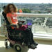 Hannah sitting in her powerchair in hospital with the city of London in the background.