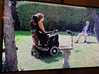 Hannah sitting in her powerchair, 2 metres apart from the journalist in her garden being interviewed.