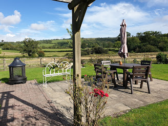 Ellwood Cottages' gardens with roses, table and chairs and grass. A view of rolling hills in the background.