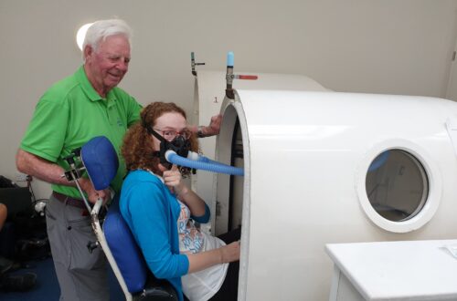 Hannah going into the hyperbaric oxygen therapy chamber. She has an oxygen mask on her face.