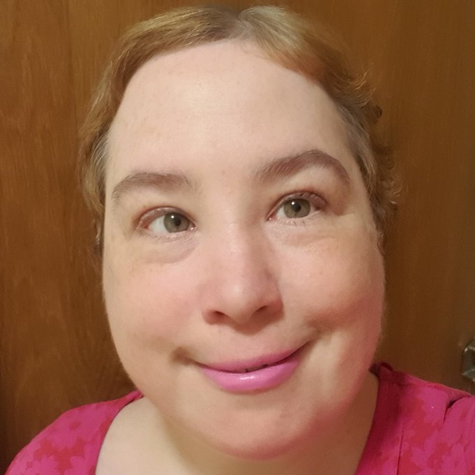 A head shot of Ciara a woman with light brown short hair, she has pink lipstick on and is wearing a bright pink top.
