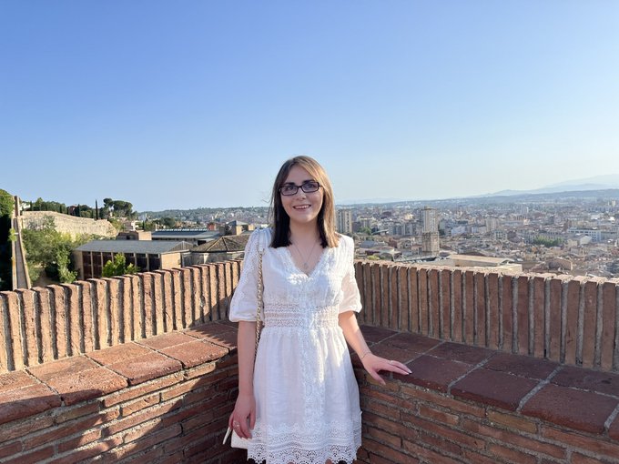 Elin is one of the disabled bloggers featured. She is a white woman with light brown hair and wearing a white dress. The skyline of a city is behind her.