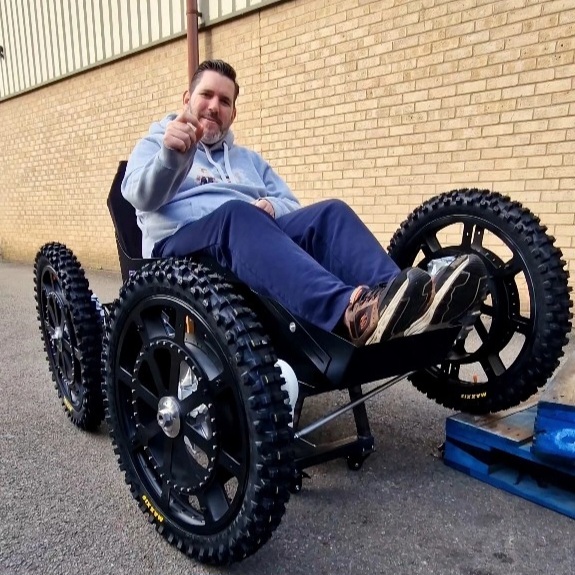 Nick Wilson in sittting in an off road wheelchair/ tramper. One wheel is off the floor.