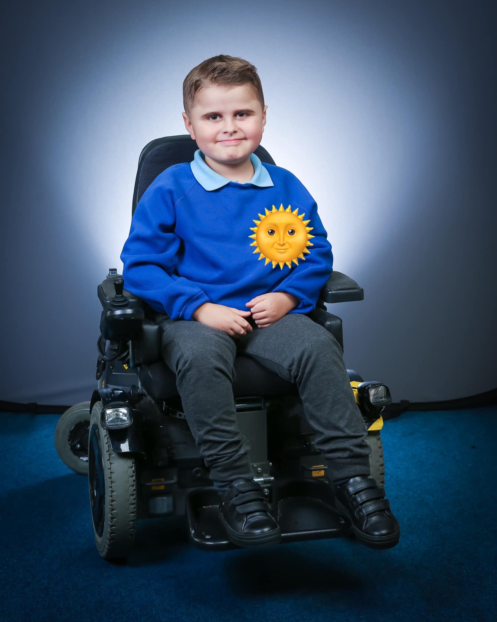 Fraser, who writes 'Fraser and Friends' a 10 year old boy, who is wearing his school uniform, grey trousers and a blue sweatshirt and sitting in his powerchair.