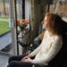 Hannah, a white woman with aburn curly hair and glasses, wearing a cream jumper with gold stripes and leggings and sitting in her powerchair. She is gazing out of the window thinking about the lessons learnt since becoming disabled.