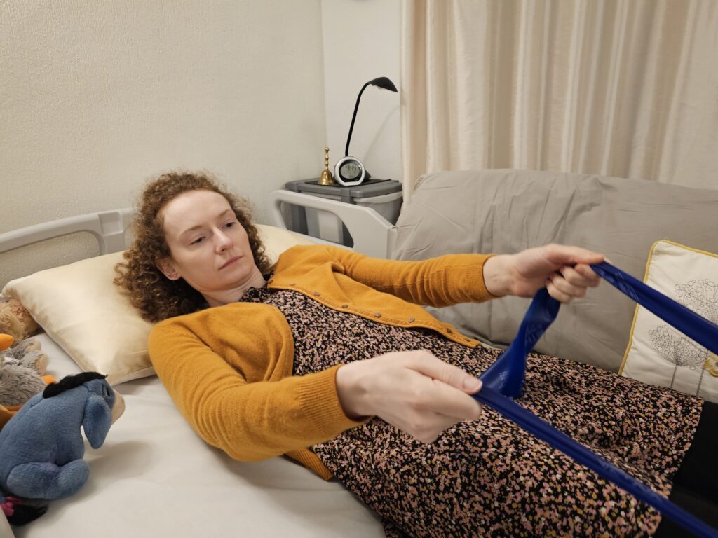 Hannah doing bed exercises with a theraband, on her electric height adjustable bed and air matress, illustrating her life.