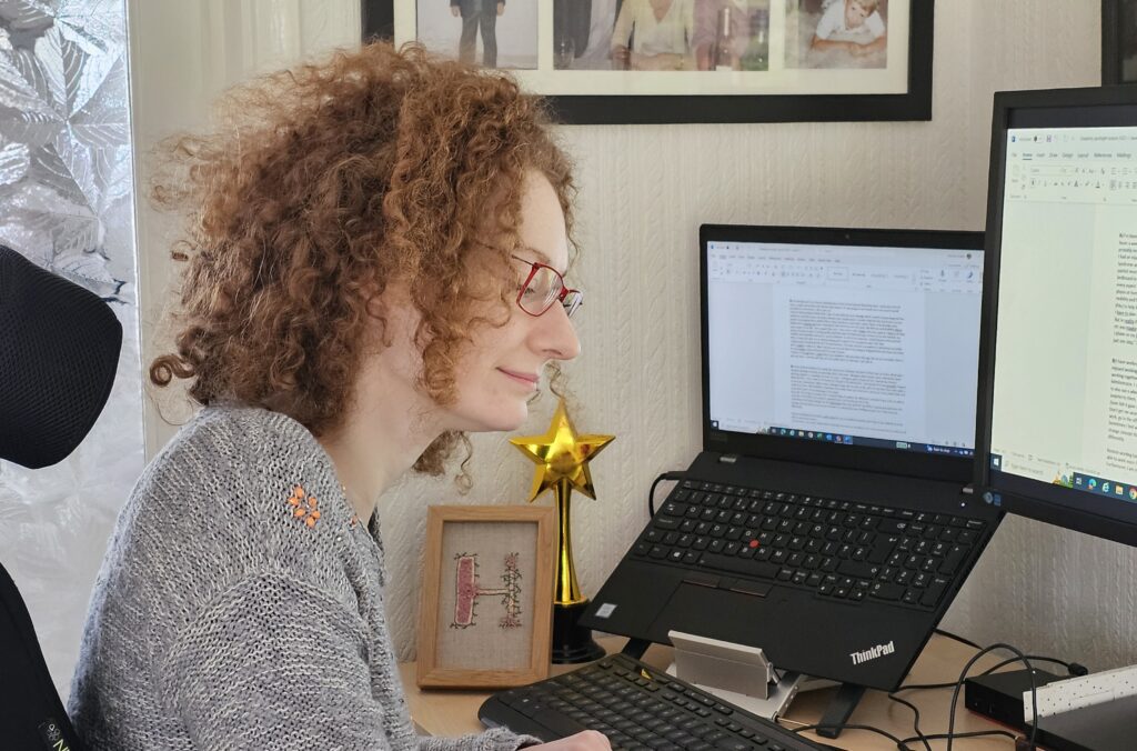 Hannah working from home. Illustrating the new flexible working law. It shows a head and shoulders shot of Hannah concentrating on her work at her desk in fromt of her laptop and monitor.