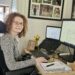 Hannah working from home, sitting at her desk with her laptop and monitor in front of her. She is turning and smiling at the camera.